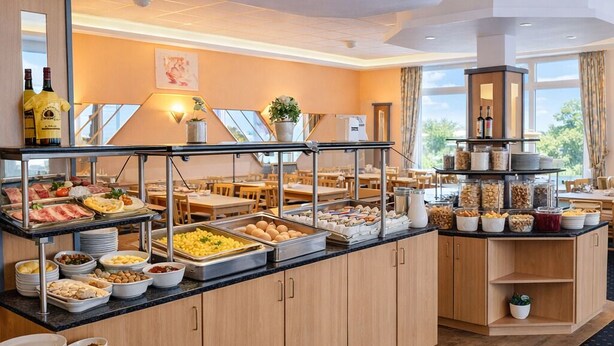 Ein reichhaltiges Buffet mit verschiedenen Speisen, eine Sitzgelegenheit und Blick durch große Fenster.