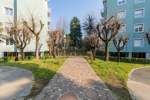 Een pad dat naar een gebouw leidt, met een bestraat voetpad, omringd door bomen en groen.