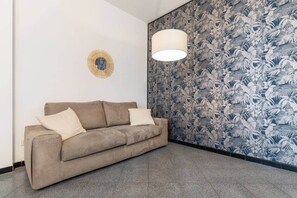 A room with a beige sofa, a round wall decoration, and a patterned wallpaper. - [M1 Cathedral] Modern retreat with terrace & BBQ (Milan)
