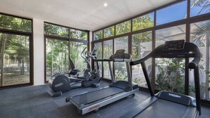 A gym with treadmills and elliptical machines, large windows, and a view of greenery. - Bright 2BR Condo | Aldea Zama (Tulum)