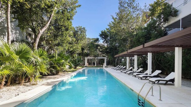 A swimming pool with lounge chairs and a pergola, surrounded by trees and greenery. - Bright 2BR Condo | Aldea Zama (Tulum)