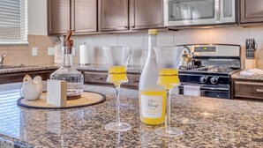 Een keukentrap met een fles 'Oceo Mango' en twee glazen gele vloeistof, een witte keramieken haan, en een kaart op een granieten aanrecht.