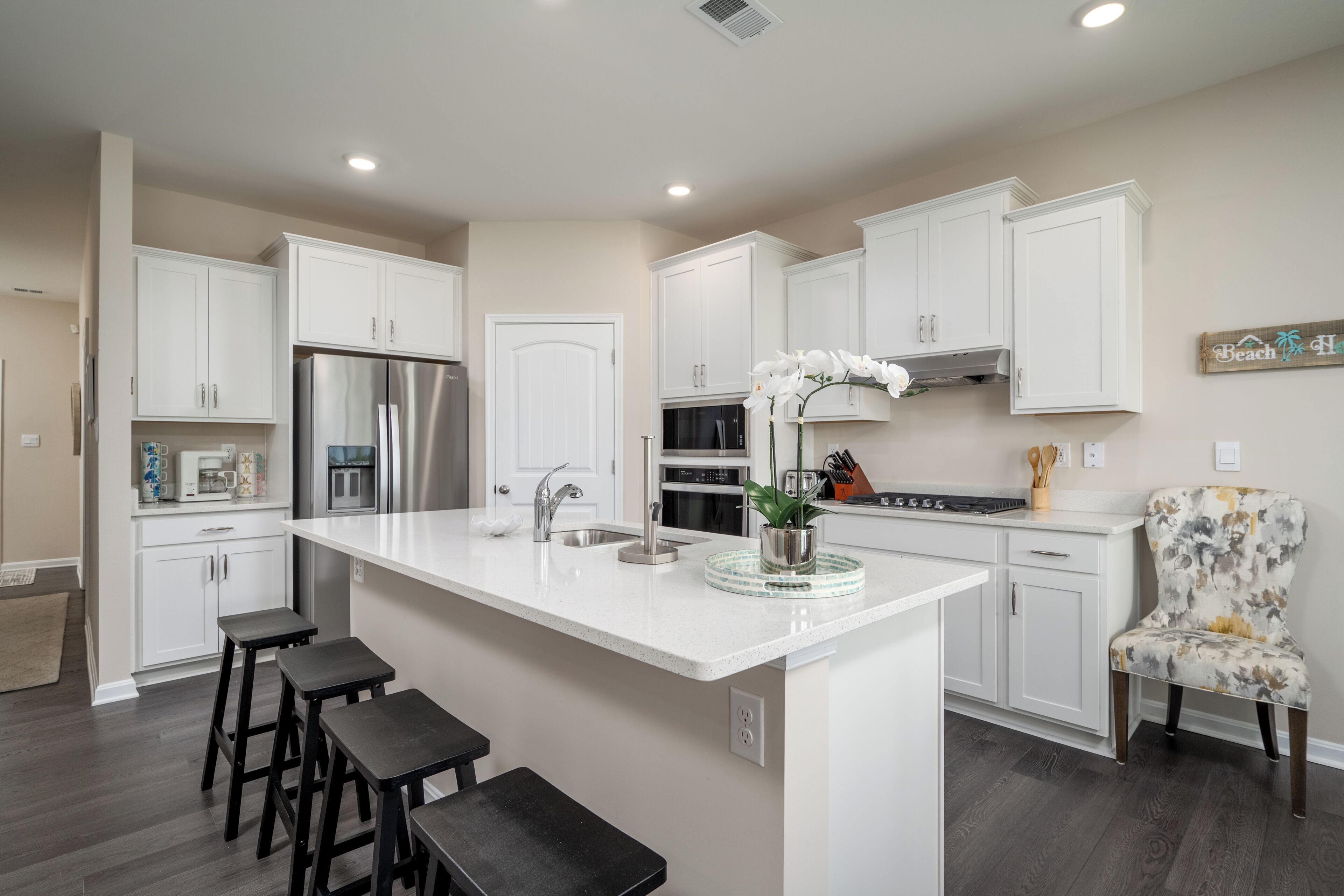 A modern kitchen with white cabinetry, a stainless steel refrigerator, a built-in oven, and a large island with bar stools.