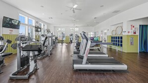 Un gimnasio con cintas de correr, máquinas de pesas y un ventilador de techo.