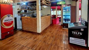 Een bar met een toonbank, planken vol flessen, een koelkast en een vitrine.