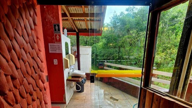 Een restaurantentree met een deurmat waarop 'Restaurante Araucária' staat, een bordje voor 'SANITÁRIOS' en een handwasstation.