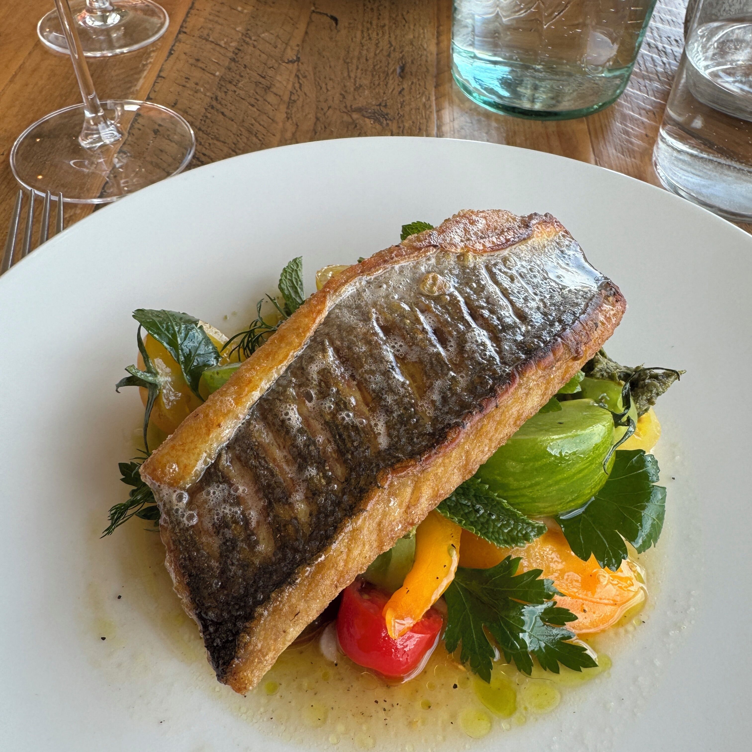 A plate with grilled fish, vegetables, and a sauce.