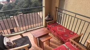 Uma varanda com uma mesa de madeira, duas cadeiras e um sofá coberto por um cobertor vermelho estampado.
