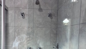 A shower area with tiled walls and multiple chrome fixtures.