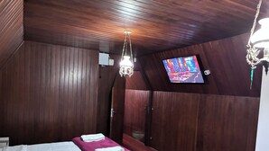 A hotel room with wooden paneling, a bed with white linens, a purple throw blanket, a chandelier, and a television on the wall.