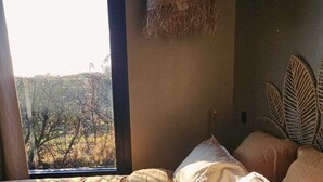 Una camera da letto con un'ampia finestra, un letto con coperta in tessuto e una testiera in vimini.