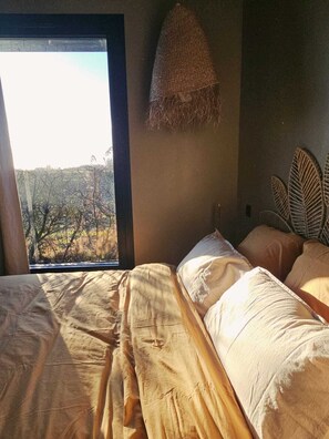 Un dormitorio con un ventanal grande, una cama con manta texturizada y un cabecero tejido.