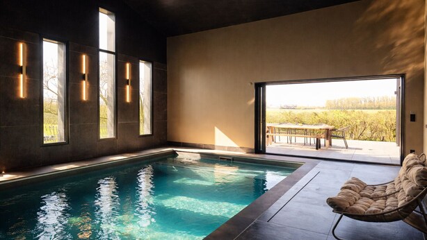 Una piscina interna moderna con vista su un vigneto, una poltrona imbottita e illuminazione integrata.