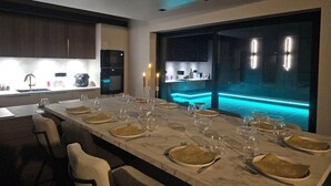 Zona pranzo moderna con un tavolo lungo apparecchiato per un pasto, angolo cottura con elettrodomestici e vista su una piscina.