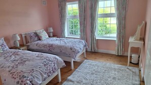 Un dormitorio con dos camas, una mesita de noche, una ventana con cortinas y una pequeña mesa blanca con lámpara.