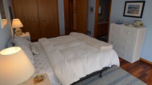 Un dormitorio con cama, mesita de noche, lámpara, cómoda y un cuadro en la pared.