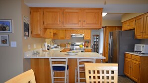 Una cocina con armarios de madera, una isla central con taburetes de bar, electrodomésticos de acero inoxidable y un microondas.