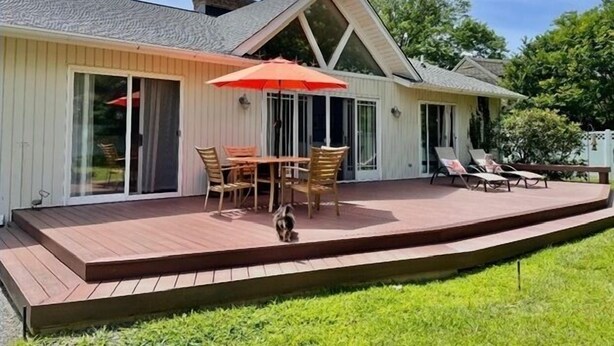 Una casa con una terraza, un comedor con sillas y una mesa, y un paraguas rojo.