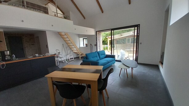 Een modern interieur met een eethoek, een blauwe bank en een trap naar een hoger gelegen verdieping.