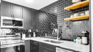 Una cocina moderna con armarios oscuros, electrodomésticos de acero inoxidable y un salpicadero de azulejos negros.