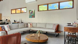 Un vaste espace de vie doté d’un plafond haut, de poutres apparentes en bois, d’une table basse ronde, d’un ensemble de canapés et d’un coin repas avec une petite table et des chaises.