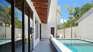 Un espace piscine extérieur moderne, offrant une vue dégagée sur le ciel, doté d’un plafond en bois et d’un coin salon avec des chaises.