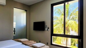 Une chambre moderne avec un grand lit, un téléviseur à écran plat fixé au mur et une fenêtre donnant sur des palmiers.