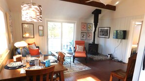 A cozy living room with a dining area, a fireplace, and a television. - Sweet cottage nestled in scenic Drummer's Cove (CS0052) (Wellfleet)