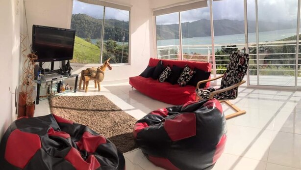Una sala de estar con un sofá rojo, un televisor y vistas a las montañas y al agua.