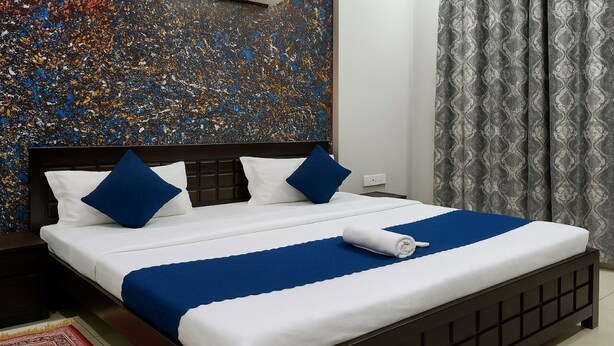 Ein ordentlich bezogenes Bett mit blau-weißer Bettwäsche, einem dunklen Kopfteil und einem gemusterten Vorhang.