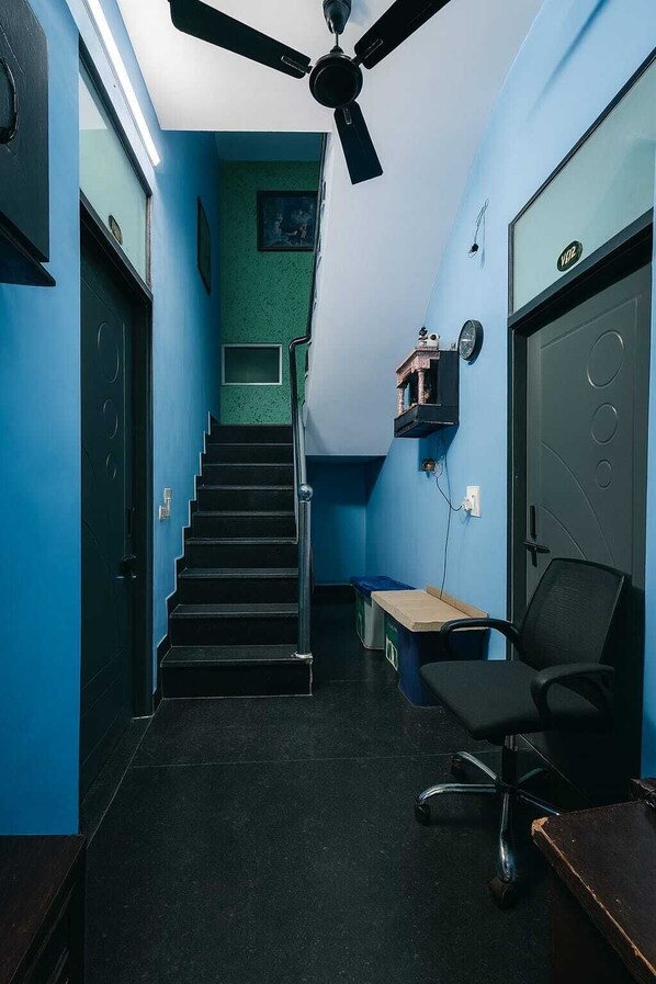 Une pièce avec un escalier, un bureau, une chaise et un ventilateur de plafond.