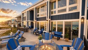 A deck with outdoor seating, a fire pit, and large windows overlooking the ocean.
