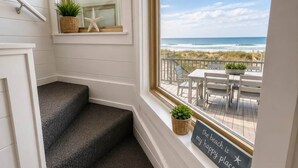 A staircase leading to a balcony with a view of the beach, a starfish decoration, and a sign that reads 'the beach is my happy place.'