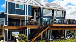 A two-story building with a wooden deck, a staircase, and a view of the beach.