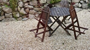 Un jardín con un muro de piedra, una mesa de madera y dos sillas.