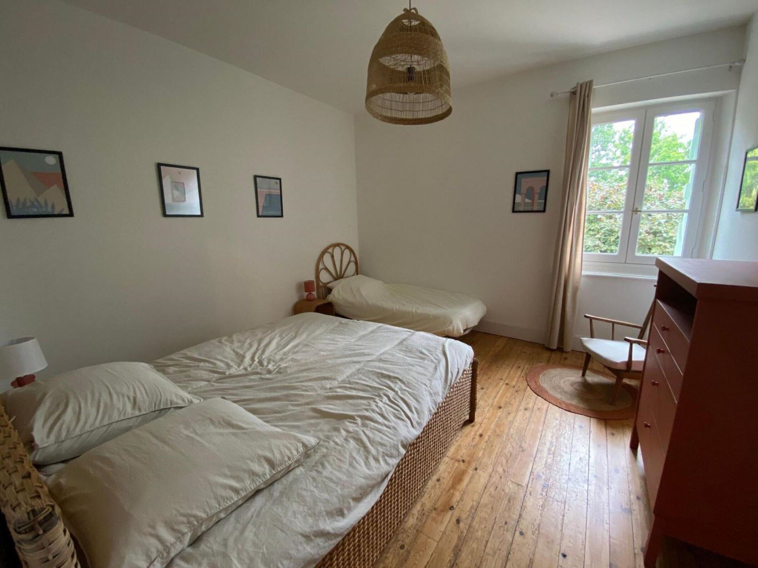 A bedroom with a bed, a chair, a dresser, and a window with curtains.