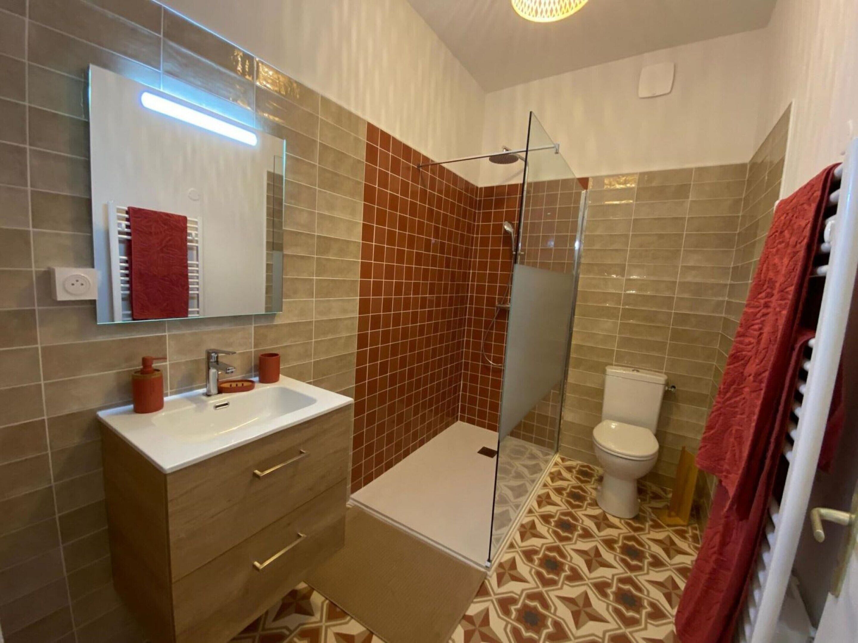 Une salle de bain moderne avec une douche à parois de verre, un lavabo blanc avec un miroir au-dessus et des toilettes.
