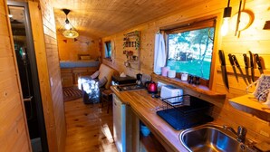 A cozy cabin interior with a wooden interior, a kitchenette with a sink and stove, a dining area with a table and chairs, and a window with a view of the outdoors. - La Vert-Dîne (Saint-Pardoux)