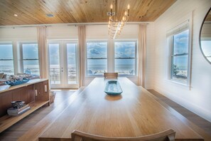 Ein geräumiger Raum mit einem großen Holztisch, einer Kandelaber und großen Fenstern mit Blick auf das Meer.