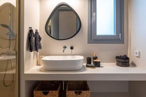 A modern bathroom with a white sink, a round mirror, and a window. - Modern Village House in Paros with Jacuzzi close to the Sea (Paros)
