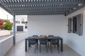 An outdoor patio with a table and chairs, a pergola overhead, and a view of a building with balconies. - Modern Village House in Paros with Jacuzzi close to the Sea (Paros)
