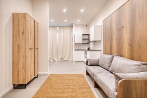A modern living room with a sofa, wooden wardrobe, and a kitchen in the background. - Hostmate - Milano - Rembrandt (Milano)