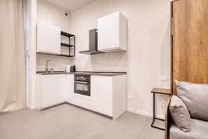 A compact kitchen with white cabinetry, a built-in oven, and a stainless steel range hood. - Hostmate - Milano - Rembrandt (Milano)