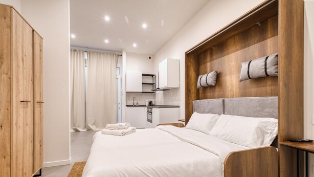 Ein Schlafzimmer mit einem Bett, einem Holzschrank und einer Küchenzeile im Hintergrund.