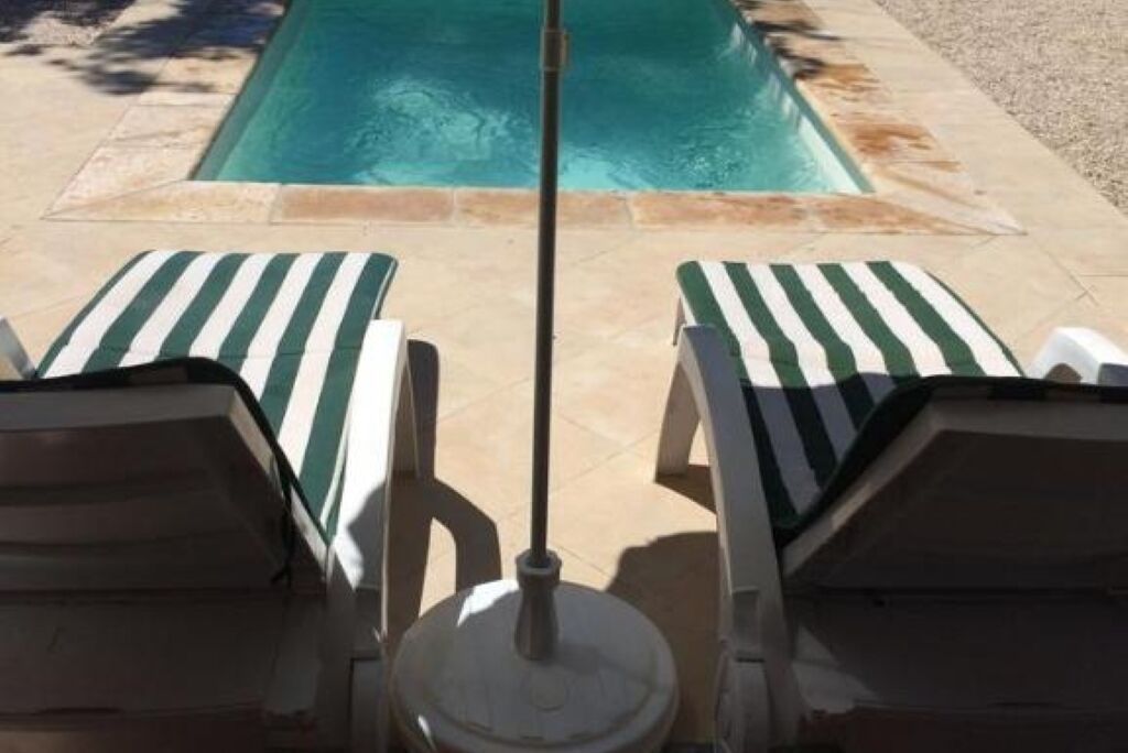 A pool area with two lounge chairs and a poolside umbrella.