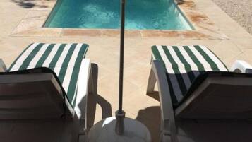 A pool area with two lounge chairs and a poolside umbrella.
