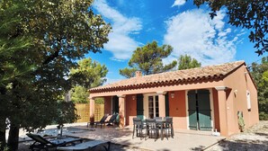 A house with a tiled roof, a patio with a table and chairs, and a covered outdoor seating area with lounge chairs.