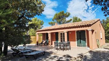 A house with a tiled roof, a patio with a table and chairs, and a covered outdoor seating area with lounge chairs.