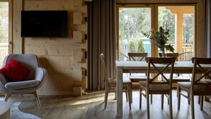 A wooden interior with a dining table, chairs, a TV mounted on the wall, and a window with a view of trees. - Comfortable Holiday Villa With Mountain Views (Zakopane)