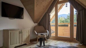 A room with a wooden ceiling, a TV mounted on the wall, a wooden cabinet, a chair, and a large window with curtains. - Comfortable Holiday Villa With Mountain Views (Zakopane)